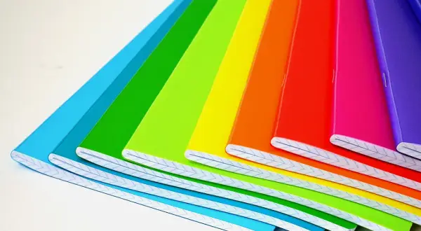 Kolorowe zeszyty ułożone w wachlarz na białym tle.